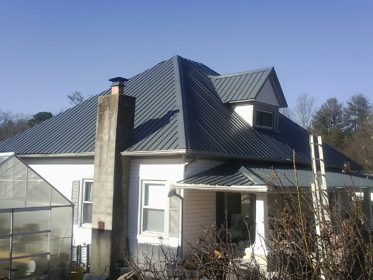 Dark blue standing seam metal roof on a white farmhouse with dormer — Slate & Tile Roof Repair by Roofing Brothers in Lewiston Woodville