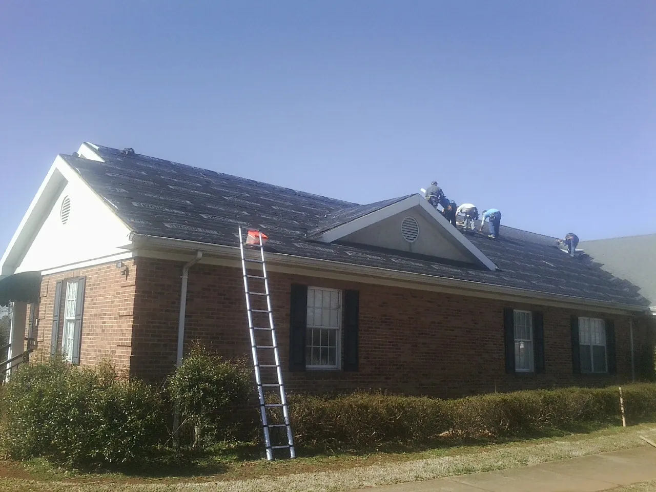 Crew tearing shingles off a brick ranch roof with a ladder set — Metal Roof Repair work by our crew in Lewiston Woodville