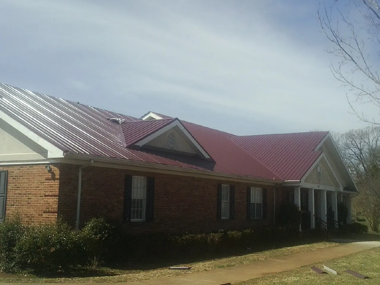 Red metal roof with gabled entries on a long brick building, from a Hail Damage Roof Repair job in Lewiston Woodville