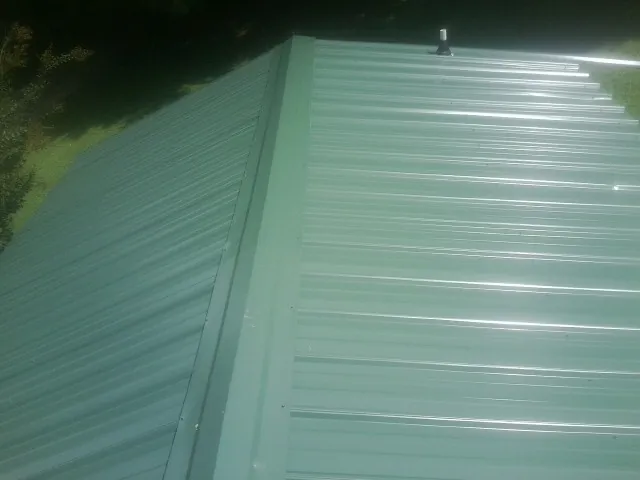 New green metal panels meeting at the ridge of a roof — Flat Roof Repair work by our crew in Lewiston Woodville