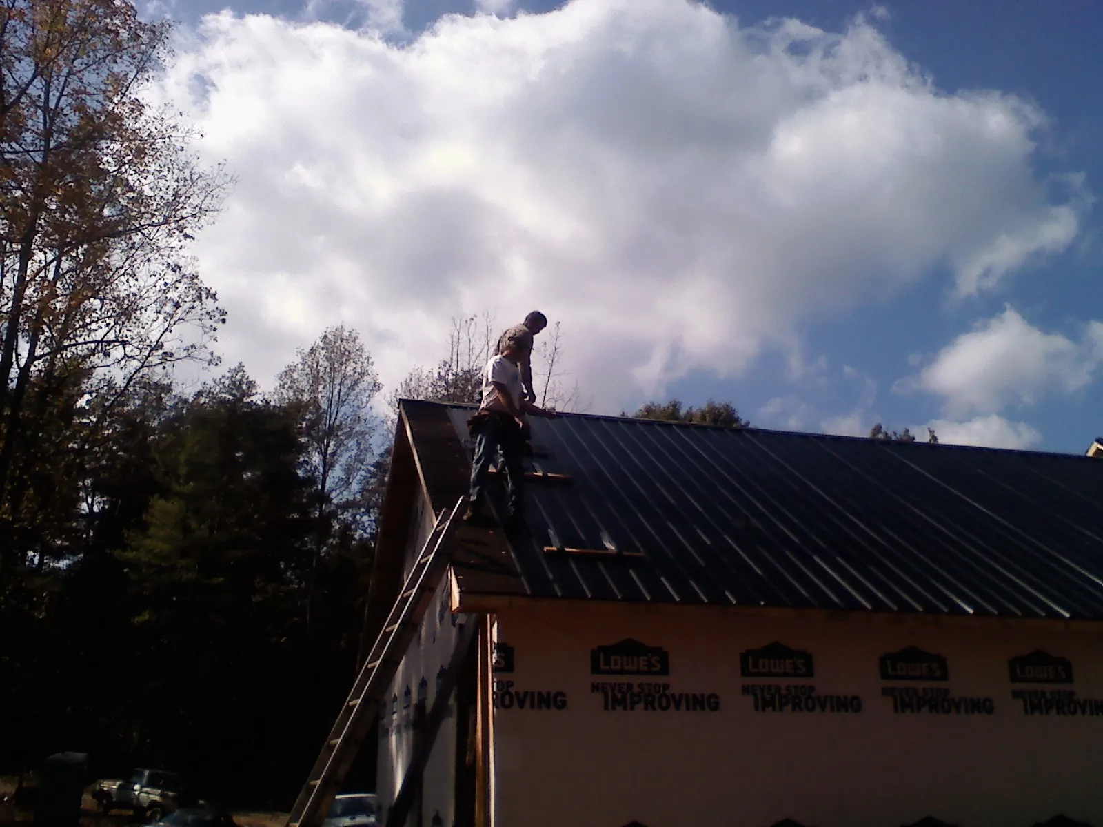 Roofer fastening dark metal panels high against a cloudy sky, from a Roof Inspection job in Lewiston Woodville