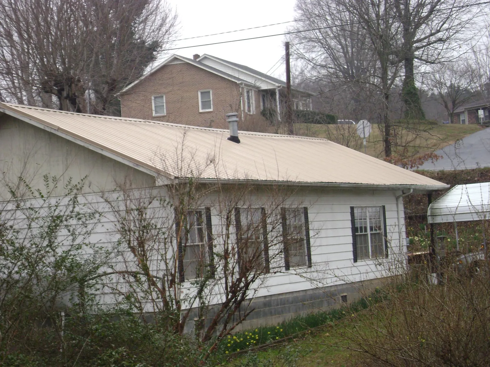 Tan metal roof on a white sided house set into a hillside — Commercial Roofing by Roofing Brothers in Lewiston Woodville