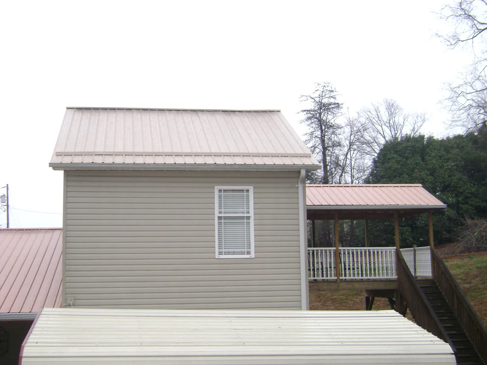 Tan metal roofs on a two story addition and attached porch, from a Roof Replacement job in Lewiston Woodville